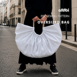Może przedstawiać: Duża, biała, obszerna torba ze złotym łańcuchem jako uchwytem. Torba jest marszczona u góry i ma czarny napis "PDF SEWING PATTERN OVERSIZED BAG". Torba jest trzymana przez osobę ubraną w czarny strój.