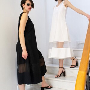 May include: Two women wearing black and white dresses with sheer panels stand on a white marble staircase. Both women are wearing sunglasses and black heeled sandals.