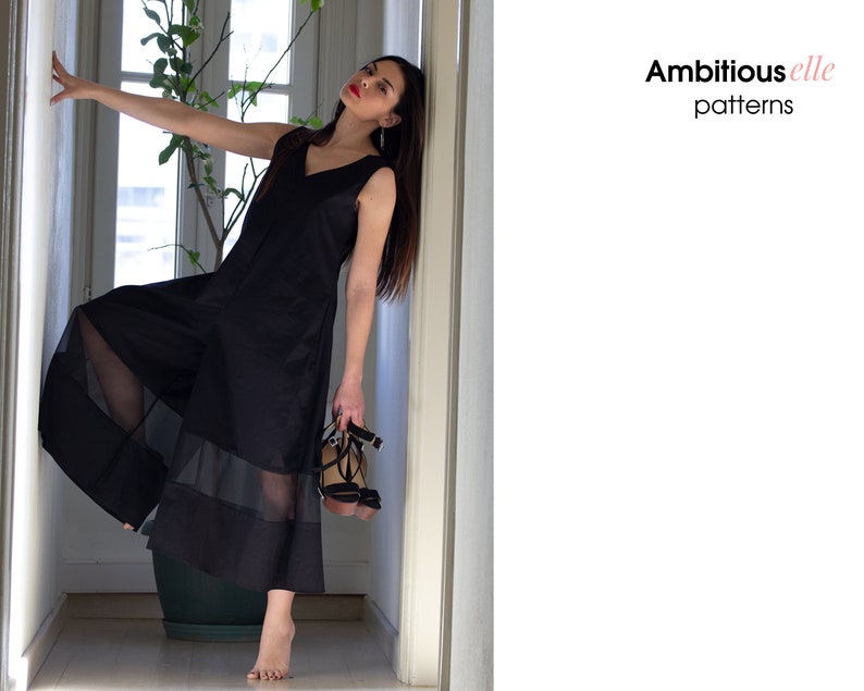 May include: A woman wearing a black sleeveless dress with sheer panels and a V-neckline. She is standing in a hallway and holding a pair of black heeled sandals. The text "Ambitious elle patterns" is visible in the upper right corner of the image.