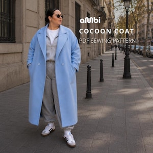 May include: A light blue cocoon coat with a double-breasted design. The coat is long and reaches the ankles. The text "AMBI COCOON COAT PDF SEWING PATTERN" is visible. The person is wearing gray sweatpants and white sneakers.