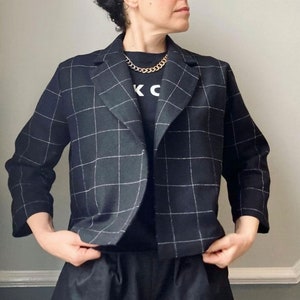 Peut inclure: Un blazer noir et blanc &agrave; carreaux avec un t-shirt noir en dessous. Le t-shirt a les lettres "K" et "C" imprim&eacute;es dessus. La personne porte un collier en cha&icirc;ne dor&eacute;e.