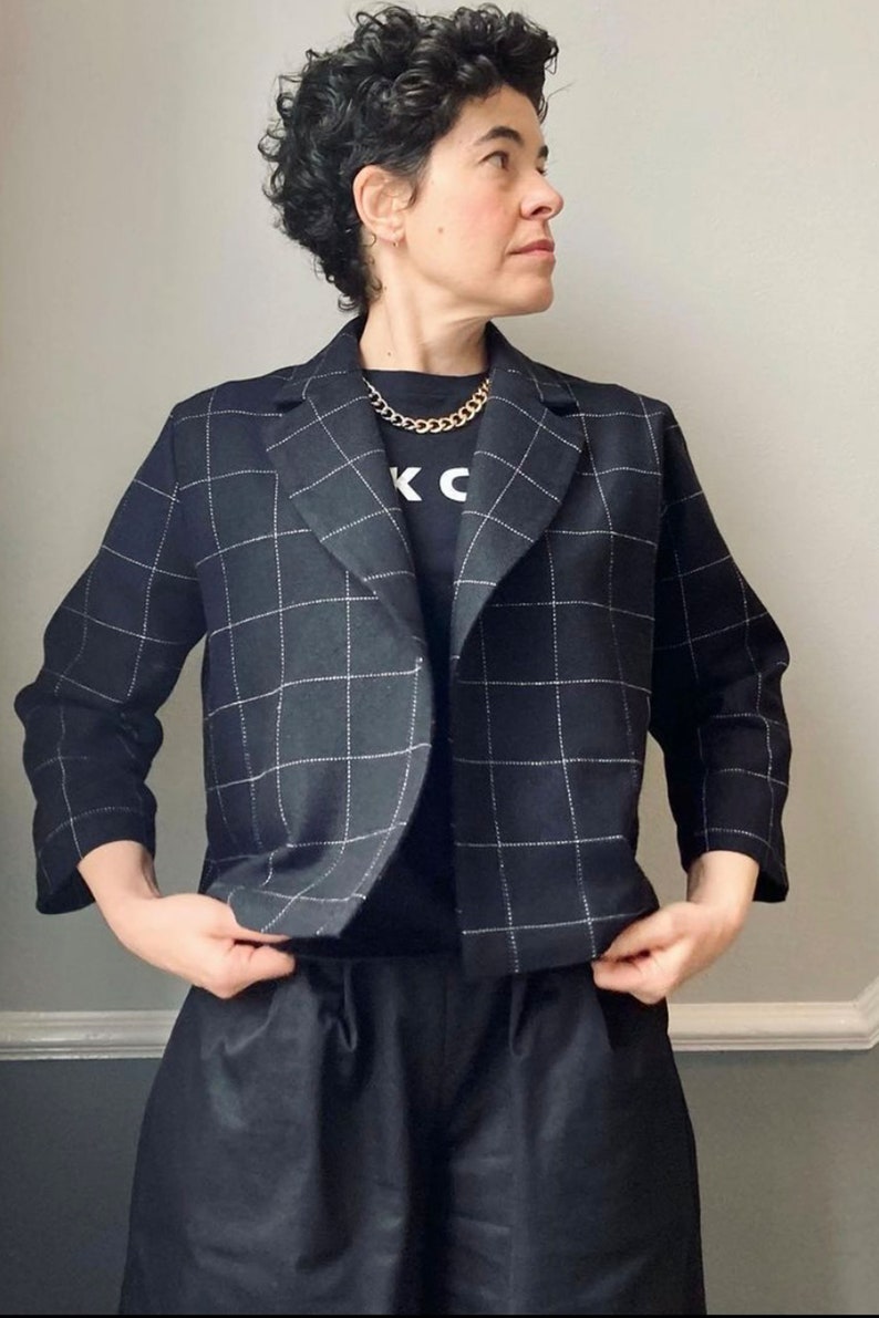 Peut inclure: Un blazer noir et blanc &agrave; carreaux avec un t-shirt noir en dessous. Le t-shirt a les lettres "K" et "C" imprim&eacute;es dessus. La personne porte un collier en cha&icirc;ne dor&eacute;e.