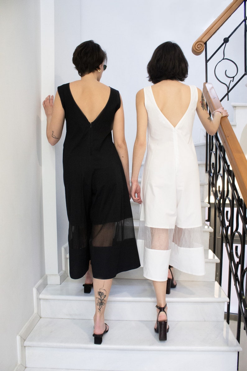 May include: Two people wearing long, sleeveless dresses with sheer panels. The person on the left is wearing a black dress and the person on the right is wearing a white dress. They are walking down a set of stairs.