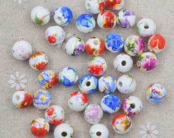 May include: A collection of white ceramic beads with floral patterns in shades of blue, red, and yellow. The beads are round and have a hole in the center for stringing.