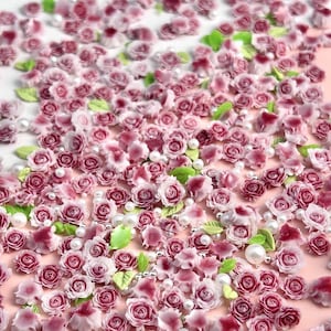 May include: A collection of small pink and white roses and leaves, with white pearl beads scattered throughout. These are perfect for adding a touch of elegance to crafts and nail art.