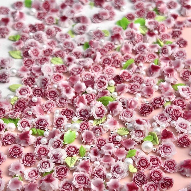 May include: A collection of small pink and white roses and leaves, with white pearl beads scattered throughout. These are perfect for adding a touch of elegance to crafts and nail art.