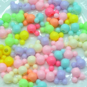 May include: A large assortment of colourful plastic beads shaped like Mickey Mouse heads. The beads are in various pastel colours, including pink, blue, yellow, green, and purple.