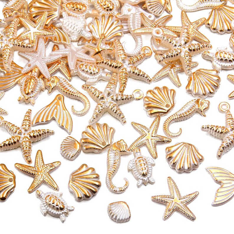 May include: A collection of gold and silver-toned seashell charms, including starfish, seahorses, and scallop shells. The charms are scattered across a white surface, creating a nautical theme. These decorative charms are ideal for jewelry making or craft projects.