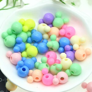May include: A collection of colourful plastic beads shaped like Mickey Mouse heads. The beads are in various pastel colours, including pink, blue, green, yellow, and purple.