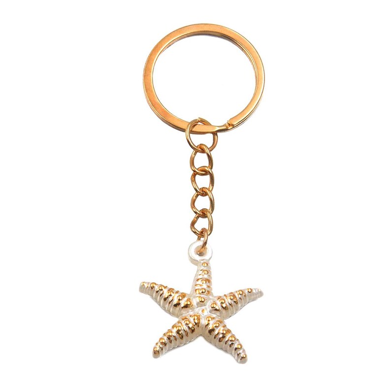 May include: Gold-colored keychain with a starfish charm. The starfish is white with gold accents, and the keychain has a gold ring and chain. The design is simple and elegant, suitable for beach lovers or those who enjoy nautical themes.