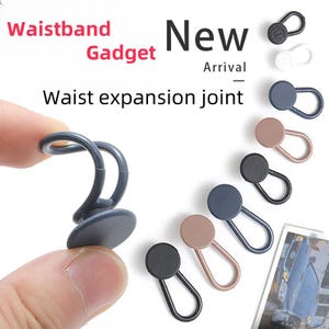 Puede incluir: Surtido de ocho extensores de cintura de plástico en varios colores, incluyendo negro, marrón, azul y gris. Los extensores están diseñados para agregar espacio adicional a los pantalones o faldas. El texto "Waistband Gadget New Arrival Waist expansion joint" es visible en la imagen.