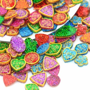 Può includere: Assortimento di decorazioni in resina glitterata di varie forme, tra cui cuori, ovali e triangoli. Le decorazioni presentano un contorno dorato e la scritta "Love" incisa su molte di esse.