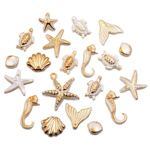 May include: A collection of gold and silver-colored sea-themed charms, including starfish, seahorses, turtles, seashells, and mermaid tails. These decorative charms are ideal for jewelry making or craft projects. The charms are arranged on a white background.