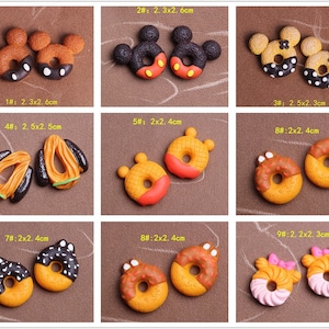 Peut inclure: Assortiment de 9 paires de breloques miniatures en forme de beignets, chacune avec un design et une couleur différents. Les beignets mesurent environ 2,5 cm de diamètre et présentent des motifs tels que des oreilles de Mickey Mouse, des pépites et du chocolat.