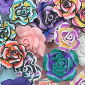 Puede incluir: Una colección de decoraciones en forma de rosa hechas a mano. Las flores presentan una variedad de colores, incluyendo amarillo, azul, rosa, morado y blanco, con detalles y patrones intrincados. Estas flores decorativas son ideales para manualidades y adornos.