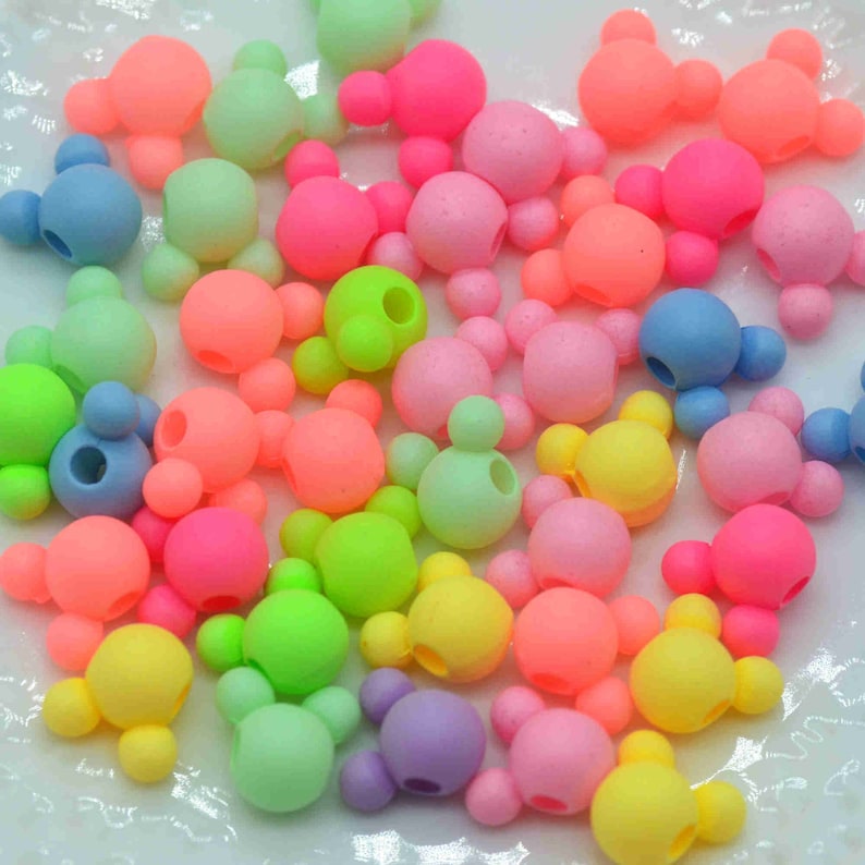 May include: A collection of colourful plastic beads shaped like Mickey Mouse heads. The beads are in various shades of pink, blue, green, yellow, and purple.