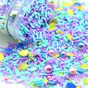 May include: A mix of pastel blue and purple sprinkles with pearl-like sprinkles and decorative seashell sprinkles.