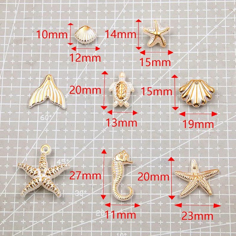 May include: A collection of gold-colored, ocean-themed charms, including a seashell (12mm), starfish (15mm and 23mm), a mermaid tail (20mm), a turtle (13mm), and a seahorse (20mm). The charms are displayed on a grid.
