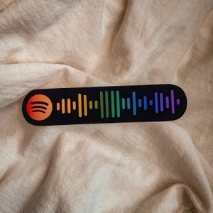 May include: A black and white sticker with a rainbow colored Spotify barcode. The sticker has a Spotify logo in the upper left corner.