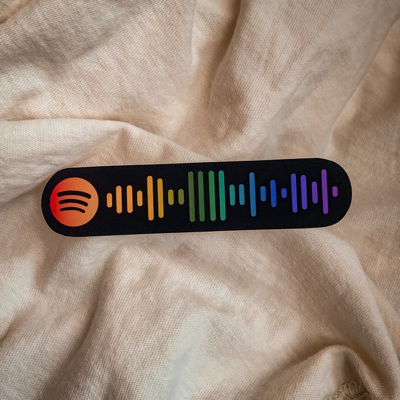 May include: A black and white sticker with a rainbow colored Spotify barcode. The sticker has a Spotify logo in the upper left corner.