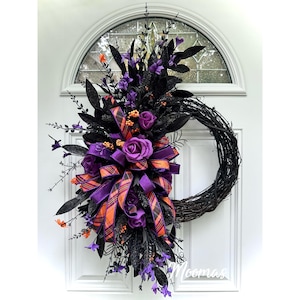 May include: A decorative wreath featuring a black twig base adorned with purple roses, black glittered foliage, and orange berry accents. A central bow made of purple and orange plaid ribbon is integrated into the arrangement of floral elements.