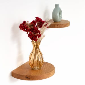 Op de afbeelding: Twee houten hoekplanken met afgeronde randen. De bovenste plank heeft een lichtblauwe vaas, en de onderste plank heeft een heldere glazen vaas met gedroogde rode bloemen.