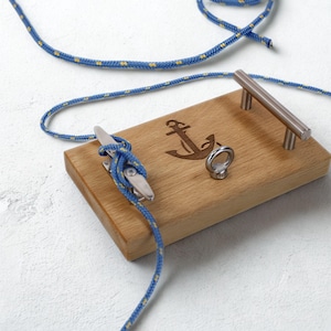 Könnte beinhalten: Holzserviertablett mit eingraviertem Ankerdesign, Metallring und Metallgriff. Blau-gelbes Seil ist an einer Klampe auf dem Tablett befestigt. Dekoration im maritimen Stil.