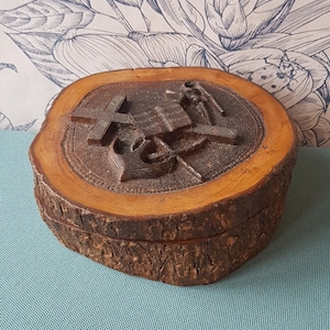 Könnte beinhalten: Eine Holzkiste mit einem geschnitzten Design aus einem Kreuz und einem Anker. Die Kiste ist aus einem Baumstamm gefertigt und hat eine natürliche Rindenoptik.