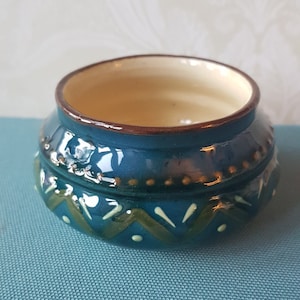 May include: A small, blue ceramic bowl with a white and green geometric design. The bowl has a brown rim and a white interior.
