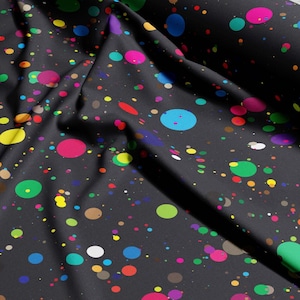 May include: Black fabric with a vibrant splatter design. The pattern includes multi-coloured circles in pink, blue, green, yellow, and brown, spread across the dark backdrop. The fabric is folded, revealing its texture and how it drapes.