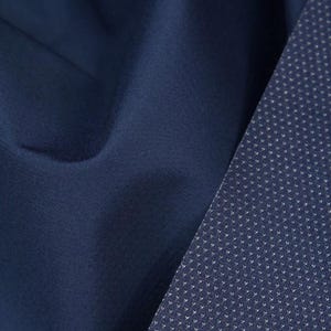 May include: Close-up of a navy blue fabric with a textured surface. A section of the fabric has a pattern of small white dots. The image shows the detail of the material.