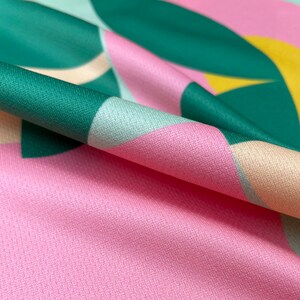 K&ouml;nnte beinhalten: Nahaufnahme eines rosa Stoffes mit einem geometrischen Muster aus gr&uuml;nen, blauen und gelben Formen. Der Stoff ist gefaltet und zeigt die Textur des Materials.