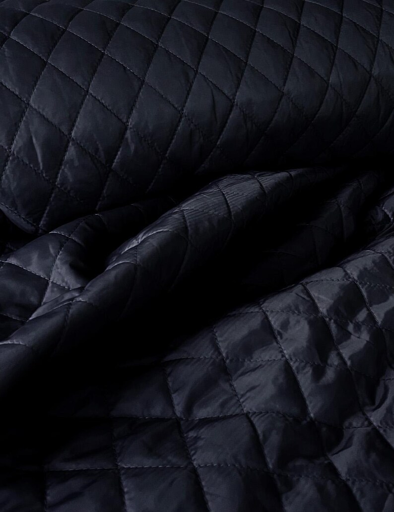 May include: Close-up of a dark blue quilted fabric with a diamond pattern. The fabric is soft and textured, with a subtle sheen.