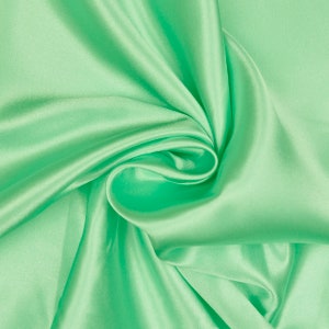 Könnte beinhalten: Ein glatter, fließender Stoff in leuchtend grüner Farbe. Der Stoff ist drapiert und gefaltet und bildet weiche, abgerundete Kurven.