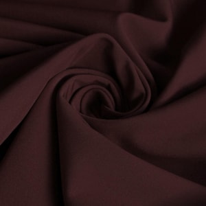 Puede incluir: Primer plano de una tela de color burdeos oscuro con una textura suave y lisa. La tela está doblada y drapeada, creando un aspecto lujoso y elegante.