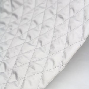 May include: A close-up of a white quilted fabric with a diamond pattern. The fabric is smooth and has a subtle sheen.