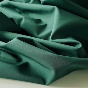 May include: A close-up of a deep green fabric with a smooth, silky texture. The fabric is folded and draped, creating soft folds and curves.