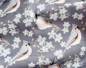 May include: Close-up of fabric with a repeating pattern of gray birds and white flowers on a gray background. The birds have gray wings, white bellies, and a small crest. The flowers have five petals and are surrounded by light green leaves.