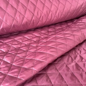 May include: A close-up of a pink quilted fabric with a diamond pattern. The fabric is soft and has a subtle sheen.