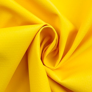 Può includere: Primo piano di un tessuto giallo brillante con pieghe morbide e una consistenza liscia. Il tessuto è stretto al centro, creando un effetto a spirale. Il colore è uniforme in tutta l'immagine, senza motivi o disegni visibili.