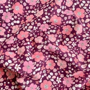 May include: Close-up of a fabric with a floral pattern. The fabric features a deep purple background with a repeating pattern of pink and light pink flowers, along with white leaves and small white flowers. The flowers have a detailed center.