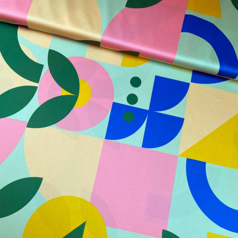 K&ouml;nnte beinhalten: Abstrakter geometrischer Musterstoff in den Farben Rosa, Blau, Gr&uuml;n und Gelb. Der Stoff hat eine Satin-Oberfl&auml;che.