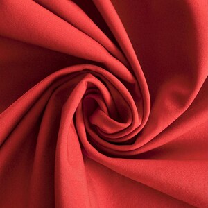 May include: A vibrant red fabric featuring a smooth, matte texture. The material is gathered into a central spiral, creating deep, flowing folds and shadows that highlight the consistent solid color and the soft, uniform surface of the textile.