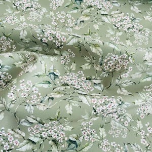 Puede incluir: Una tela verde con un estampado floral blanco. Las flores son pequeñas y delicadas, y la tela tiene una textura suave y fluida.