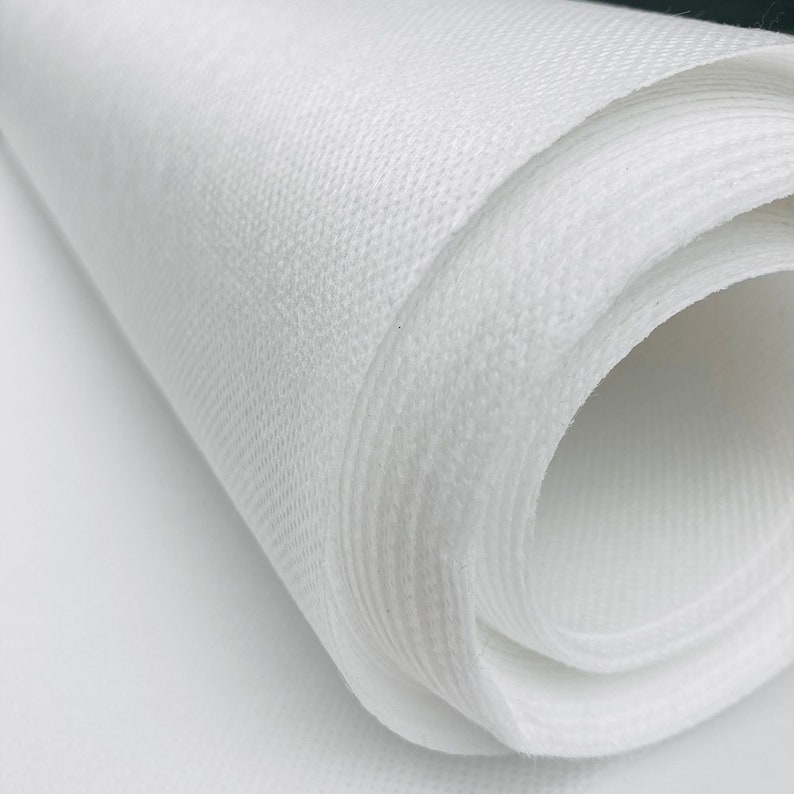 May include: Close-up of a roll of white fabric. The fabric has a textured, woven appearance and is tightly rolled, revealing the layers. The material appears soft and lightweight, suitable for various crafting or sewing projects.