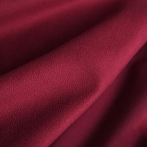 May include: A close-up shot of a deep burgundy fabric with a soft, textured surface. The material is draped, creating folds and shadows that highlight its plush appearance. The colour is a rich, saturated shade of red.