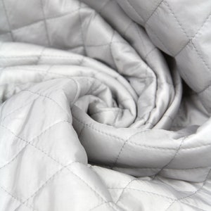 May include: Close-up of a white quilted fabric with a diamond pattern. The fabric is folded and twisted, creating a soft and textured look.