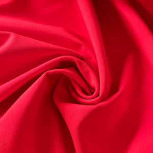 May include: A close-up of a bright red fabric with soft folds and wrinkles.