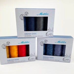 May include: Three boxes of Mettler Denim Doc thread spools. Each box has a different color scheme, including shades of blue, yellow, orange, and red. The boxes are light blue with the Mettler logo and product information printed on them.