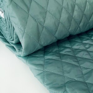 May include: A roll of teal quilted fabric with a diamond pattern. The fabric is folded in half and the edges are visible.